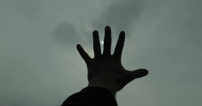 Extending hand towards cloudy gloomy sky with sun hardly visible through the la&iacute;er of clouds