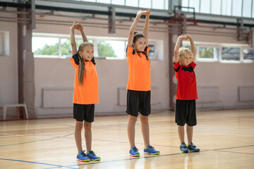 Three kids doing stretching on PE lesson