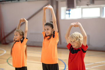 Three kids in bright tshirts doing stretching in the gym