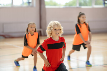 Three kids exercising in the gym and doing lungings forward