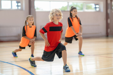 Kids exercising in the gym and doing lungings forward