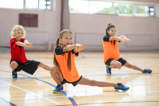 Three Kids Exercising In The Gym And Doing Lungings To The Left