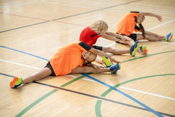 Three kids in bright sportswear sitting on the floor and stretching