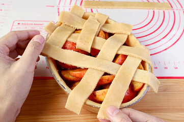 Hand weaving pieces of cut dough on pie plate for lattice top crust of a homemade apple pie