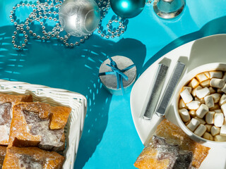 Christmas breakfast with coffee, marshmallows, cookies, chocolate, gift, and decorations on blue table