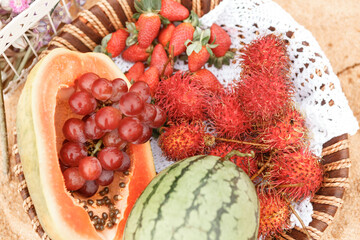 Obraz na płótnie Canvas Picnic background with basket with tropical fruits - watermelon, papaya, strawberries and rambutan on sandy bach