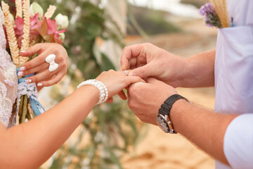 Beauty bride and handsome groom are wearing rings each other during the ceremony on the beach, close up