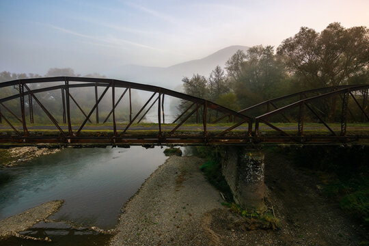 abandoned metal bridge in morning fog. dangerous construction in autumnal countryside scenery at sunrise