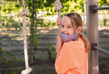 happy child girl on playground in face mask. epidemic, virus