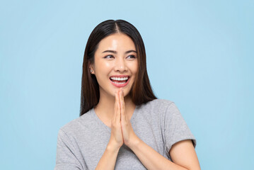 Smiling beautiful Asian woman doing Wai gesture for greeting or thank you isolated on light blue background