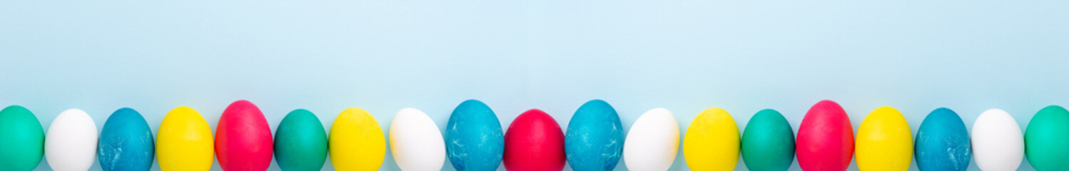 Extra long horizontal banner with multicolored easter eggs on blue background. Easter concept. Copy space
