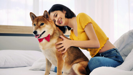 Happy woman and shiba inu dog lying together on a bed at home