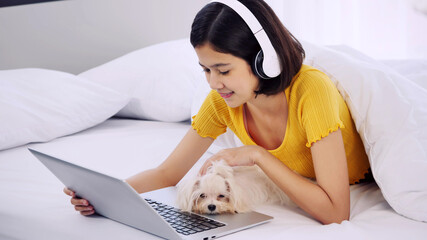 Asian woman using a laptop computer and lying on a bed with shihtzu dog