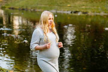 Thoughtful pregnant woman walking near lake at autumn.