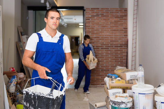 Glad positive man and woman in work overalls doing finishing work in room of public space