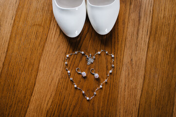 Women's shoes, necklace and earrings on wooden brown background. Bride accessories. Top view.