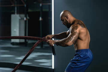 Side view of powerful athlete doing exercises with rope in modern gym