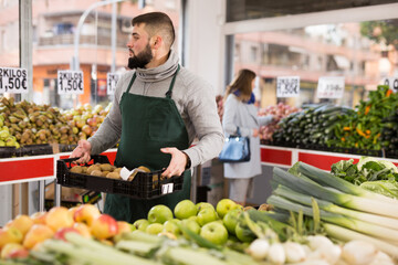 Man seller moving box of kiwi in grocery shop. High quality photo