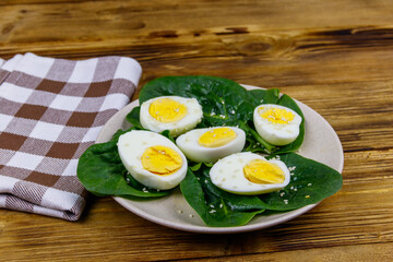 Boiled eggs with fresh spinach leaves and sesame seeds on wooden table