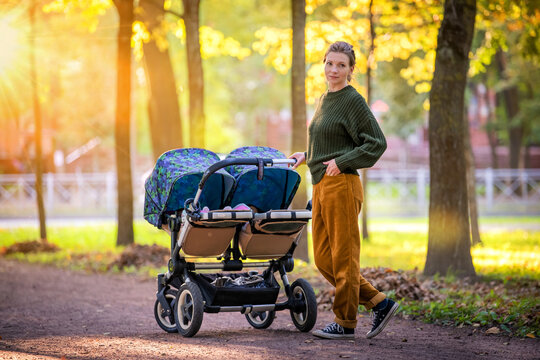 Happy mom are walking in autumn park with a stroller for twins. Full-length portrait.