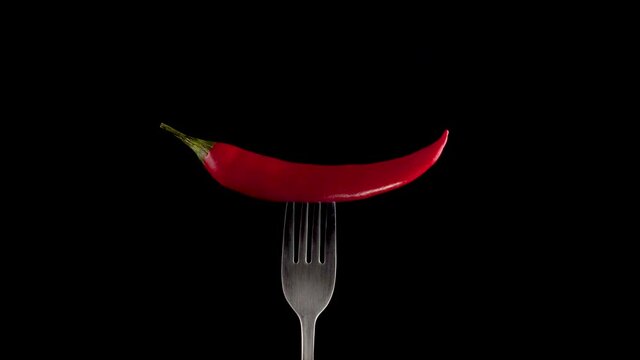 Hot red chili pepper on the fork rotates on a black background. Spicy food concept. Close up 4K