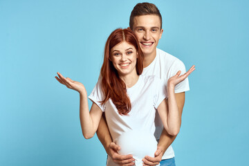 Pregnant woman in white t-shirt and man married couple waiting for baby blue background cropped view of emotions