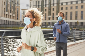 Young couple in sports clothing wearing protective masks running along the street during training