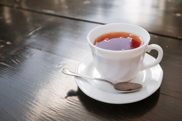 Cup with black tea onwooden background. White ceramic cup, place for text.
