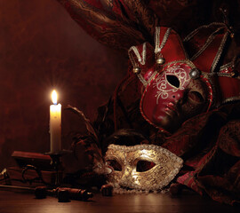 Carnival masks, dice and small brass candlestick with burning candle.