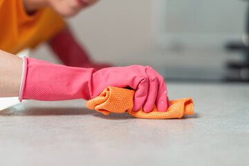 Cleaning the house. A woman in pink rubber gloves diligently wipes the kitchen countertop with a rag. Hands close up