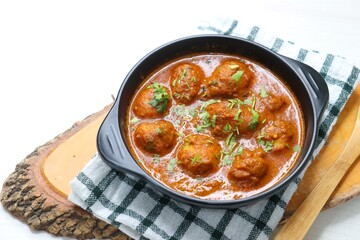 Indian cuisine - Kashmiri Dum Aloo or Potatoes in red gravy over white background. Garnished with coriander. Serve hot with rice or Naan/roti. Copy space. Panjabi Dam alu curry.