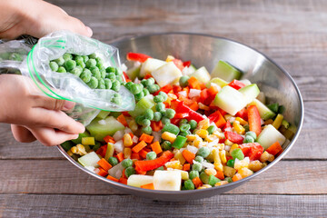 Frozen mix of vegetables and green peas in a bag on wooden table