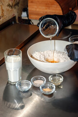 Baking a cake in a rural kitchen - a recipe for a dough made from the ingredients of eggs, flour, milk, yeast, sugar on a shiny table. The egg is added to the flour