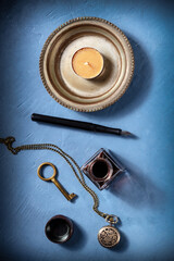 Vintage objects, the concept of nostalgia, a flat lay with an old watch, ink pen and well, and a candle, shot from the top on a blue background