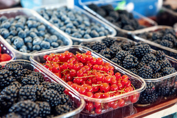 Blueberries, strawberries, raspberries and blackberries are prepared for sale at the farmers ' market. Fruits on the market counter are laid out in plastic containers. Fresh farm products.