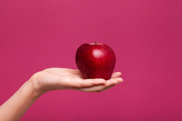 Young woman hold fresh red apple in hand besides bordo background