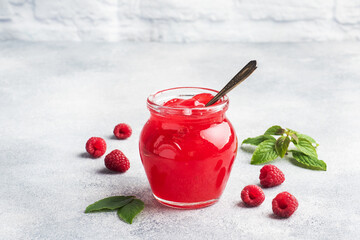 Homemade raspberry jam in a glass jar and fresh raspberries with mint on a grey concrete background. Copy space