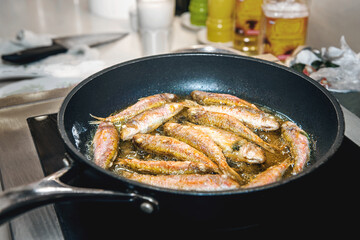 Small fish of barabul and horse mackerel are fried in oil in a frying pan on an induction cooker