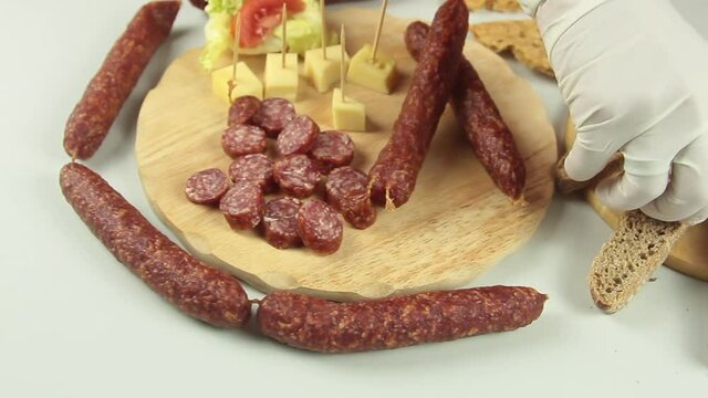 slider view of chefs hands serving a typical South Tyrolean snack plate like Tyrolean smoked sausage on a wooden cutting board accompanied by kaminwurz and paarl type bread