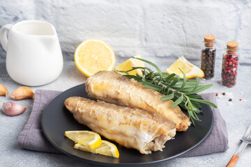 Fried fish hake Pollock and slices of fresh lemon. grey concrete background. Copy space.