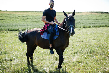 Arab tall beard man wear in black and sunglasses ride arabian horse.