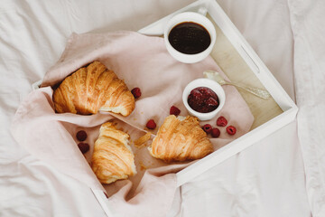Morning breakfast in bed, coffee and croissant on the tray.