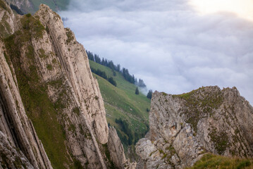 Colorful sunrise on the clouds and steep ridge of the majestic  Schaefler peak in the Alpstein mountain range Appenzell, Switzerland with the fog in the valley rolling over the hills