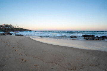 footprints in the sand at sunset with slow shutter to show the wave movement in the background, room for text