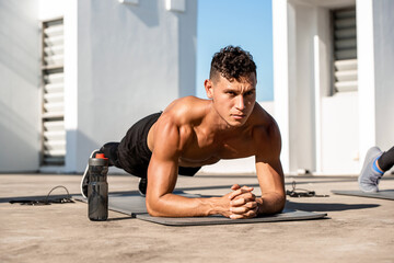 Shirtless muscular sports man doing plank workout exercise in the open air on building rooftop floor