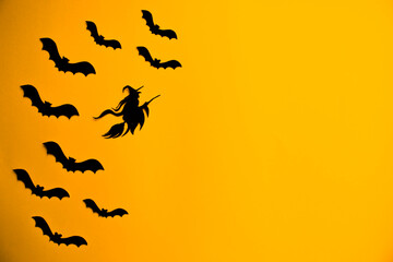 Silhouettes of black bats and witch on broomstick. Halloween paper decorations on orange background. Funnyy Halloween greeting banner with copy space. Flat lay for your design.