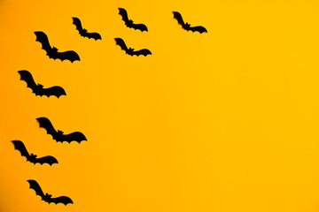Silhouettes of black bats made of paper on orange background. Halloween greeting template with copy space. Flat lay for your design.