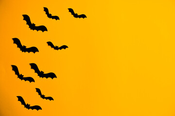 Silhouettes of black bats made of paper on orange background. Halloween greeting template with copy space. Flat lay for your design.