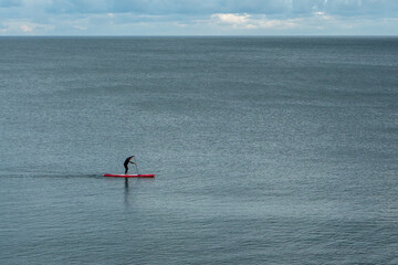 A man paddle boarding on the Devon coastline. Landscape image with mostly deep blue sea filling the frame. Copy space available