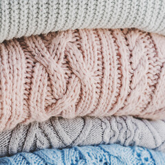 Fototapeta na wymiar Pile of warm knitted sweaters of pastel colors. Knitwear for cold autumn and winter season